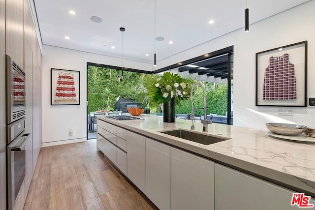 kitchen featuring sink, light hardwood / wood-style flooring, appliances with stainless steel finishes, light stone counters, and decorative light fixtures