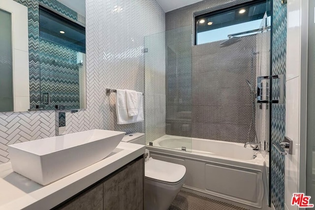 full bathroom featuring shower / bath combination with glass door, vanity, toilet, and tile walls