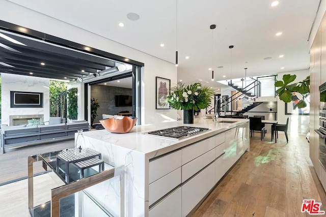 kitchen with white cabinetry, hanging light fixtures, a large island with sink, stainless steel gas stovetop, and light hardwood / wood-style floors