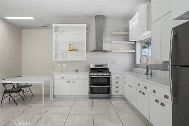 kitchen featuring light tile patterned floors, wall chimney range hood, stainless steel appliances, and white cabinetry