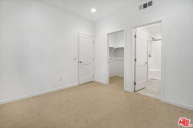 unfurnished bedroom featuring light colored carpet, a closet, connected bathroom, and a spacious closet