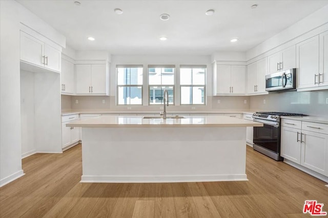 kitchen featuring a center island, stainless steel appliances, light wood-type flooring, white cabinetry, and sink