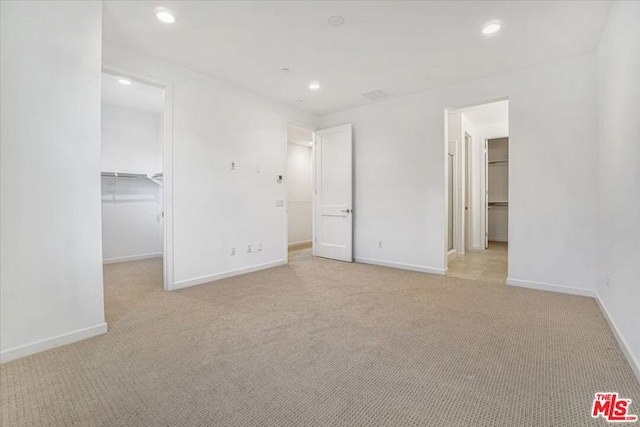 unfurnished bedroom with a walk in closet, a closet, and light colored carpet