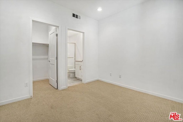 unfurnished bedroom with a closet, a spacious closet, light carpet, and connected bathroom