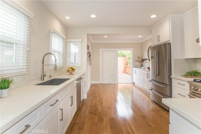 kitchen with high end appliances, white cabinetry, a healthy amount of sunlight, and sink