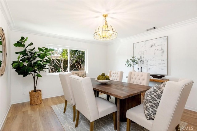 dining area with an inviting chandelier, ornamental molding, and light hardwood / wood-style flooring