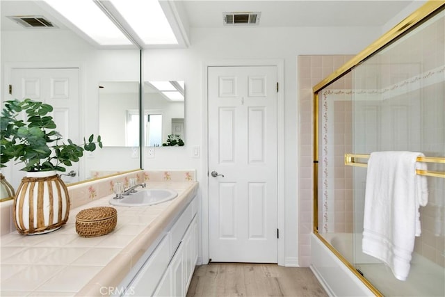 bathroom with hardwood / wood-style floors, vanity, and enclosed tub / shower combo