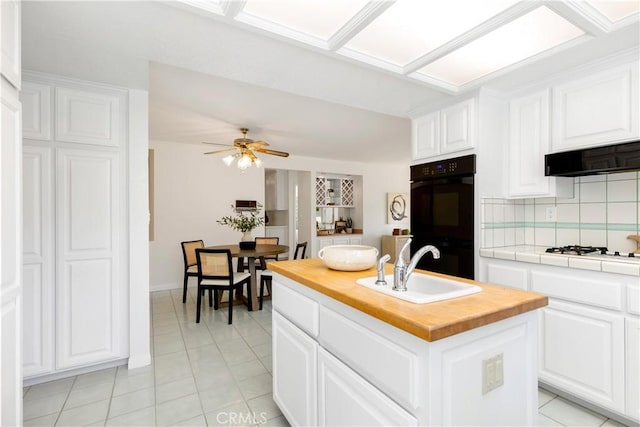 kitchen with black double oven, white cabinetry, a kitchen island with sink, and butcher block countertops