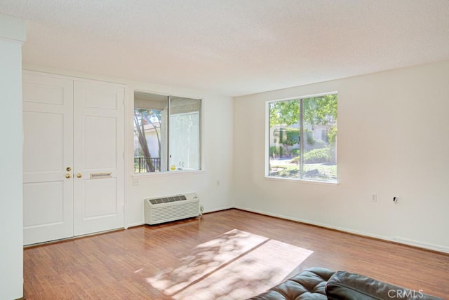 unfurnished room with a wall unit AC, a textured ceiling, and hardwood / wood-style flooring