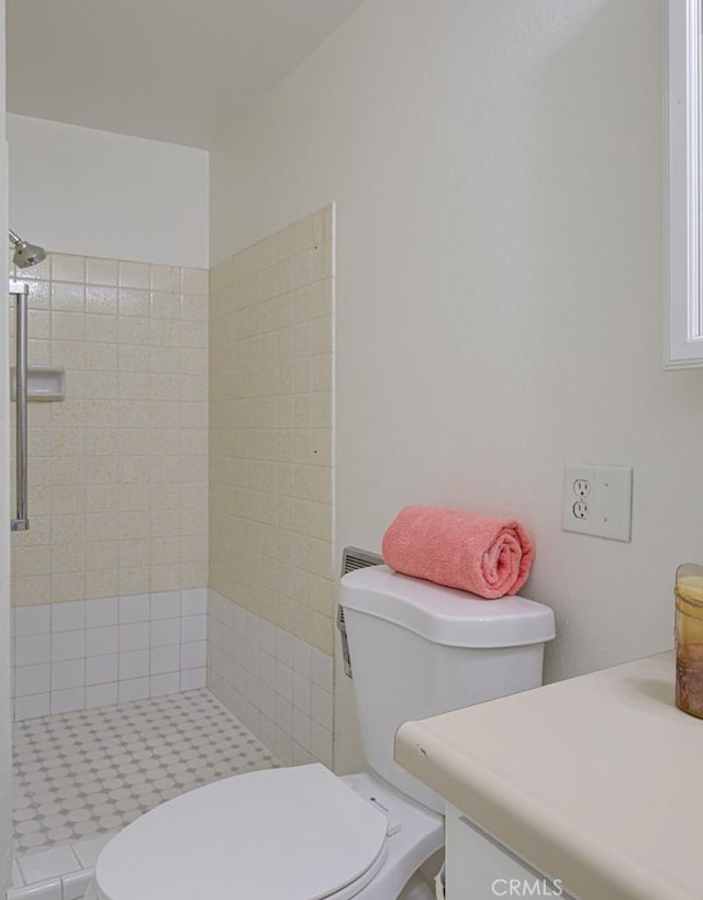 bathroom with toilet, a tile shower, and vanity