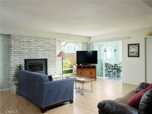 living area with light wood-style flooring, a fireplace, baseboards, and a textured ceiling