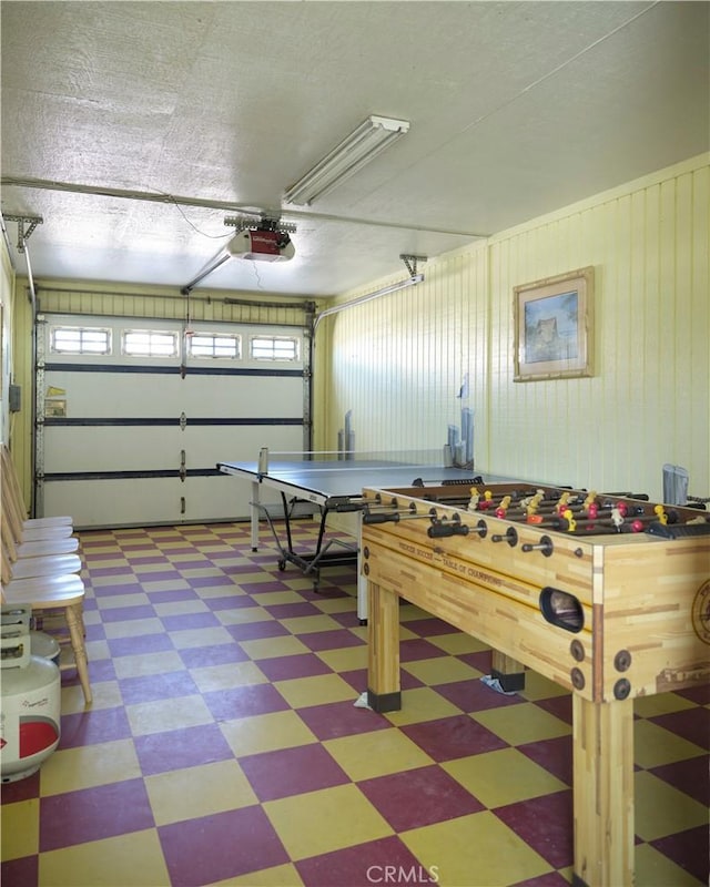 rec room featuring a garage, light floors, and a textured ceiling