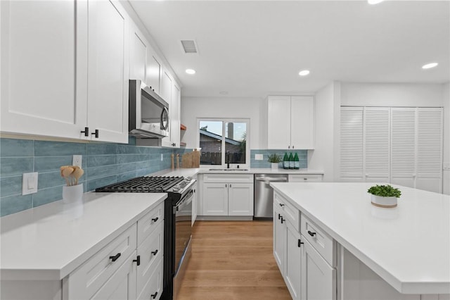 kitchen with white cabinets, sink, decorative backsplash, light wood-type flooring, and appliances with stainless steel finishes