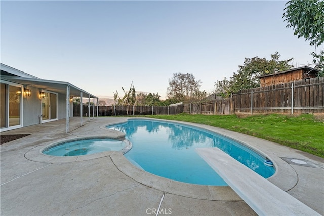 pool at dusk featuring a patio area, an in ground hot tub, a yard, and a diving board