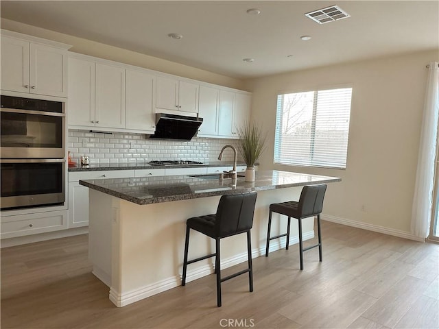 kitchen featuring white cabinets, a center island with sink, and sink