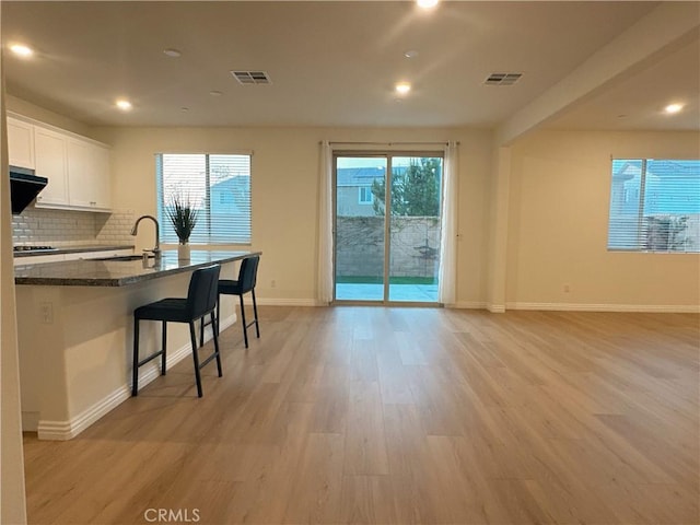 kitchen featuring light hardwood / wood-style floors, a kitchen breakfast bar, dark stone countertops, white cabinets, and sink