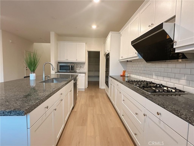 kitchen with a center island with sink, sink, white cabinetry, light hardwood / wood-style flooring, and appliances with stainless steel finishes