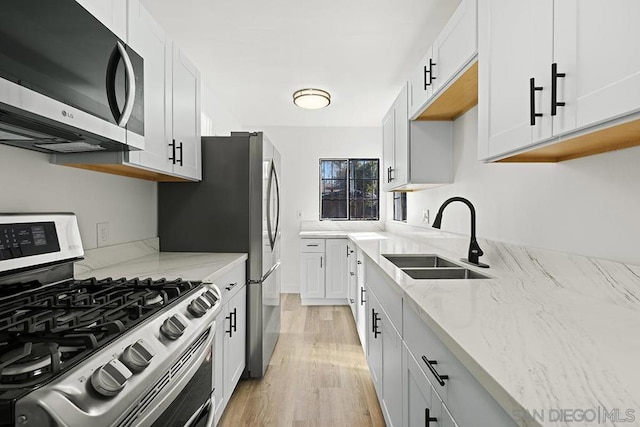 kitchen featuring stainless steel appliances, white cabinets, light stone countertops, light hardwood / wood-style flooring, and sink