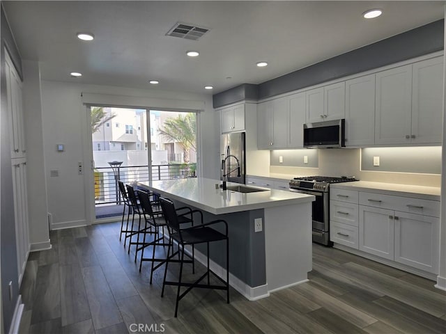 kitchen with a kitchen bar, an island with sink, stainless steel appliances, white cabinets, and sink