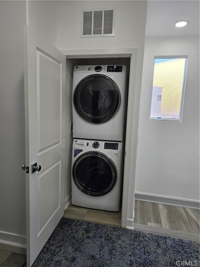 clothes washing area with stacked washer and dryer and hardwood / wood-style flooring