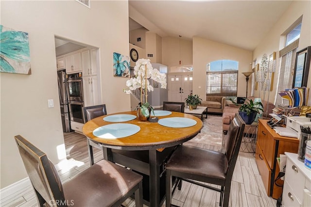 dining space featuring high vaulted ceiling and light hardwood / wood-style flooring