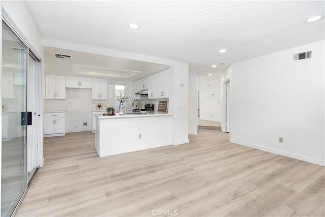 kitchen with white cabinetry, a textured ceiling, light wood-type flooring, stainless steel range, and kitchen peninsula