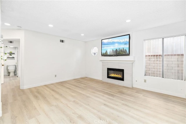 unfurnished living room with a tile fireplace, a textured ceiling, and light hardwood / wood-style flooring