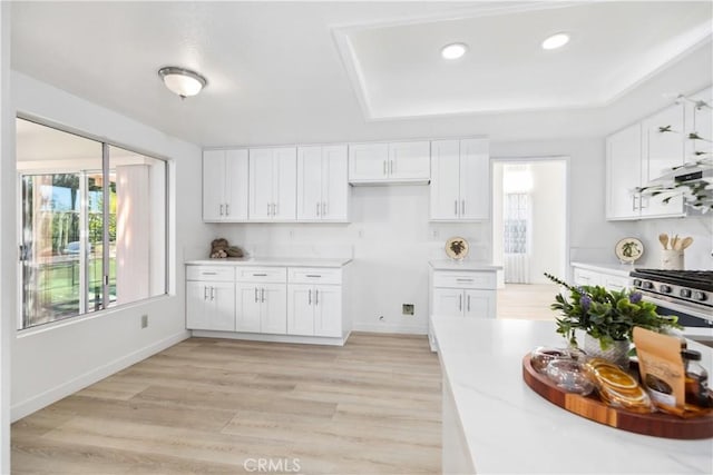 kitchen with a raised ceiling, stainless steel range with gas stovetop, white cabinets, and light hardwood / wood-style flooring