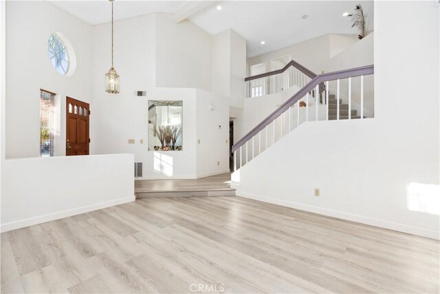 interior space featuring light wood-type flooring, beam ceiling, and a towering ceiling