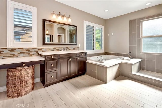 bathroom with a garden tub, vanity, a wealth of natural light, and decorative backsplash