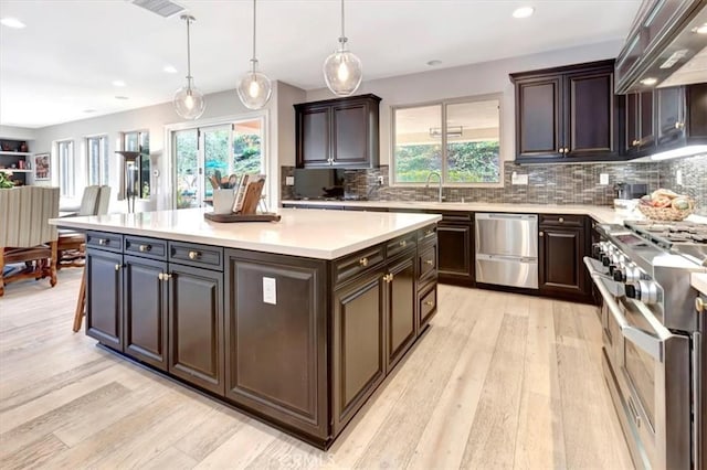 kitchen with light countertops, appliances with stainless steel finishes, dark brown cabinets, a center island, and pendant lighting