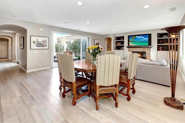 dining space featuring built in shelves, arched walkways, visible vents, and light wood finished floors