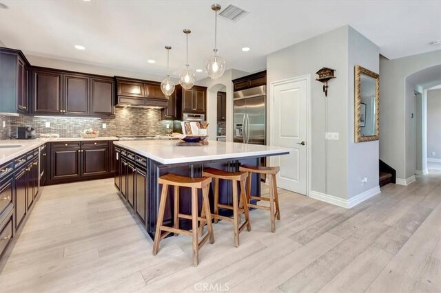 kitchen with dark brown cabinetry, decorative light fixtures, a kitchen island, stainless steel appliances, and light hardwood / wood-style floors