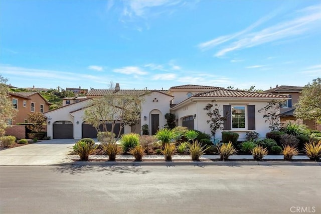 mediterranean / spanish house featuring driveway, a tiled roof, an attached garage, and stucco siding