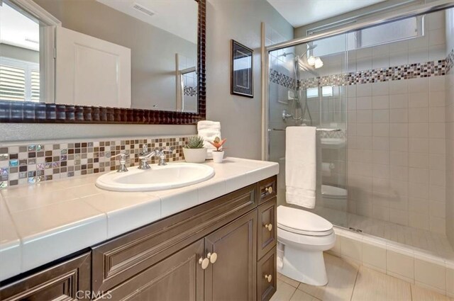 bathroom with tasteful backsplash, tile patterned flooring, vanity, an enclosed shower, and toilet