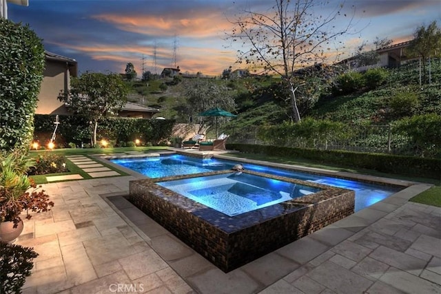 pool at dusk featuring a patio and an in ground hot tub