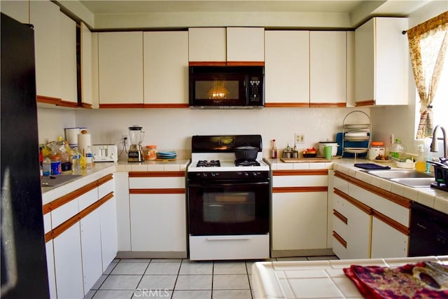 kitchen featuring tile countertops, light tile patterned flooring, white cabinetry, and black appliances