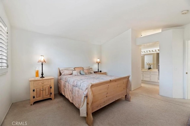 bedroom with ensuite bathroom, light colored carpet, and vaulted ceiling