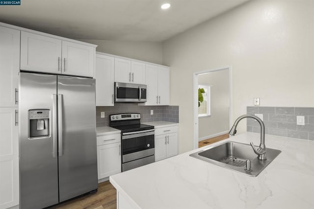 kitchen featuring light stone countertops, appliances with stainless steel finishes, white cabinetry, sink, and vaulted ceiling