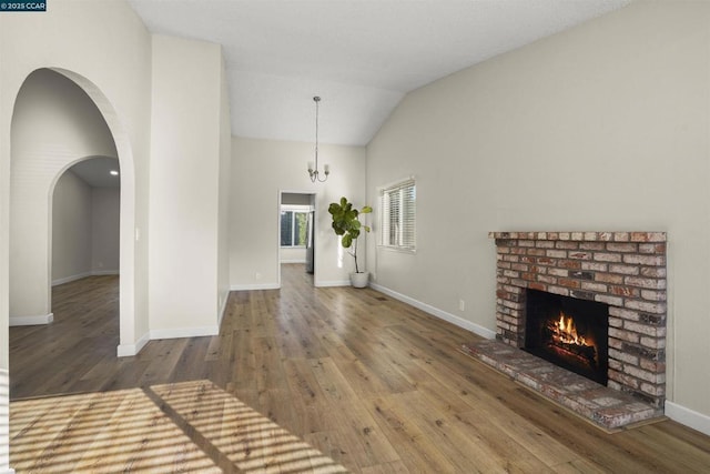 unfurnished living room with a brick fireplace, wood-type flooring, lofted ceiling, and a notable chandelier