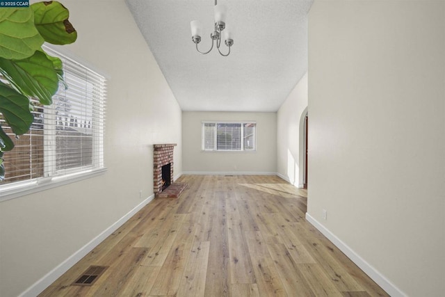 unfurnished living room with light hardwood / wood-style flooring, plenty of natural light, a chandelier, and a brick fireplace