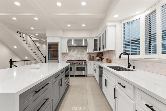 kitchen with stainless steel appliances, wall chimney exhaust hood, white cabinets, and light stone counters