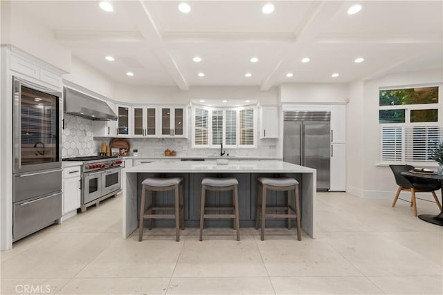 kitchen featuring premium appliances, wall chimney exhaust hood, white cabinetry, and a center island