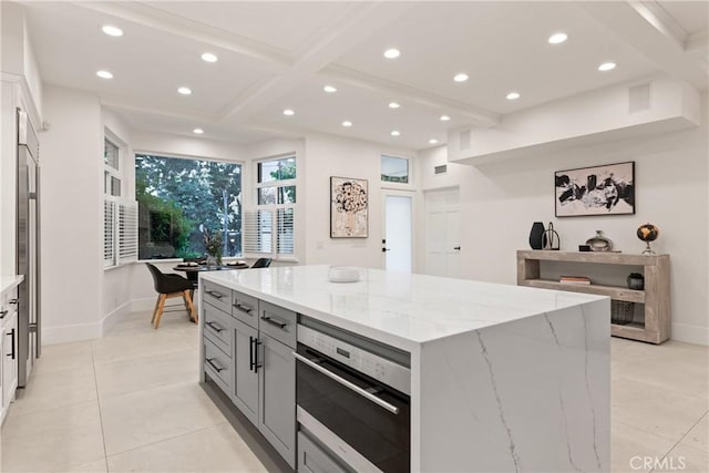 kitchen featuring gray cabinetry, a spacious island, light tile patterned flooring, light stone countertops, and beam ceiling