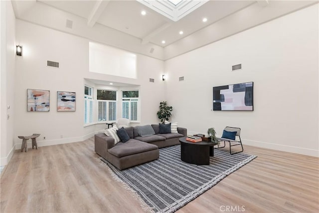 living room featuring beam ceiling, light wood-type flooring, and a high ceiling