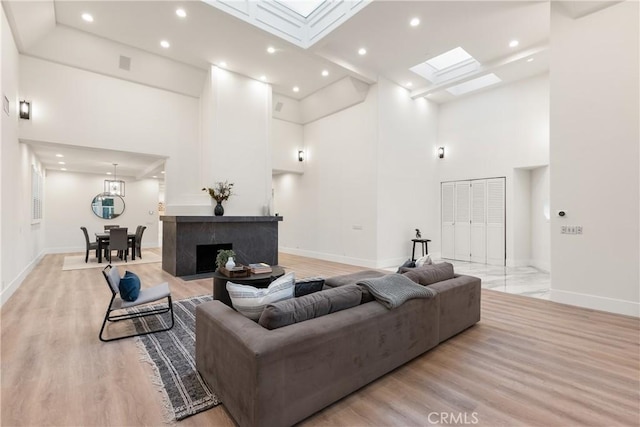 living room with a fireplace, a skylight, light hardwood / wood-style floors, and a towering ceiling