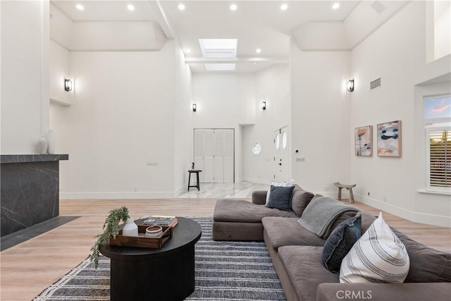 living room featuring light wood-type flooring, a skylight, and a high ceiling