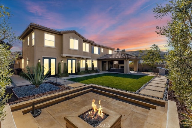 back house at dusk featuring an outdoor fire pit, a gazebo, a patio area, and a yard