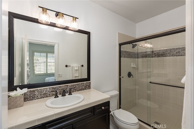 bathroom with toilet, vanity, backsplash, and a shower with door