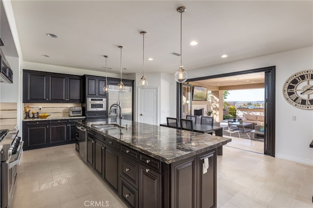 kitchen featuring dark stone countertops, pendant lighting, sink, appliances with stainless steel finishes, and an island with sink